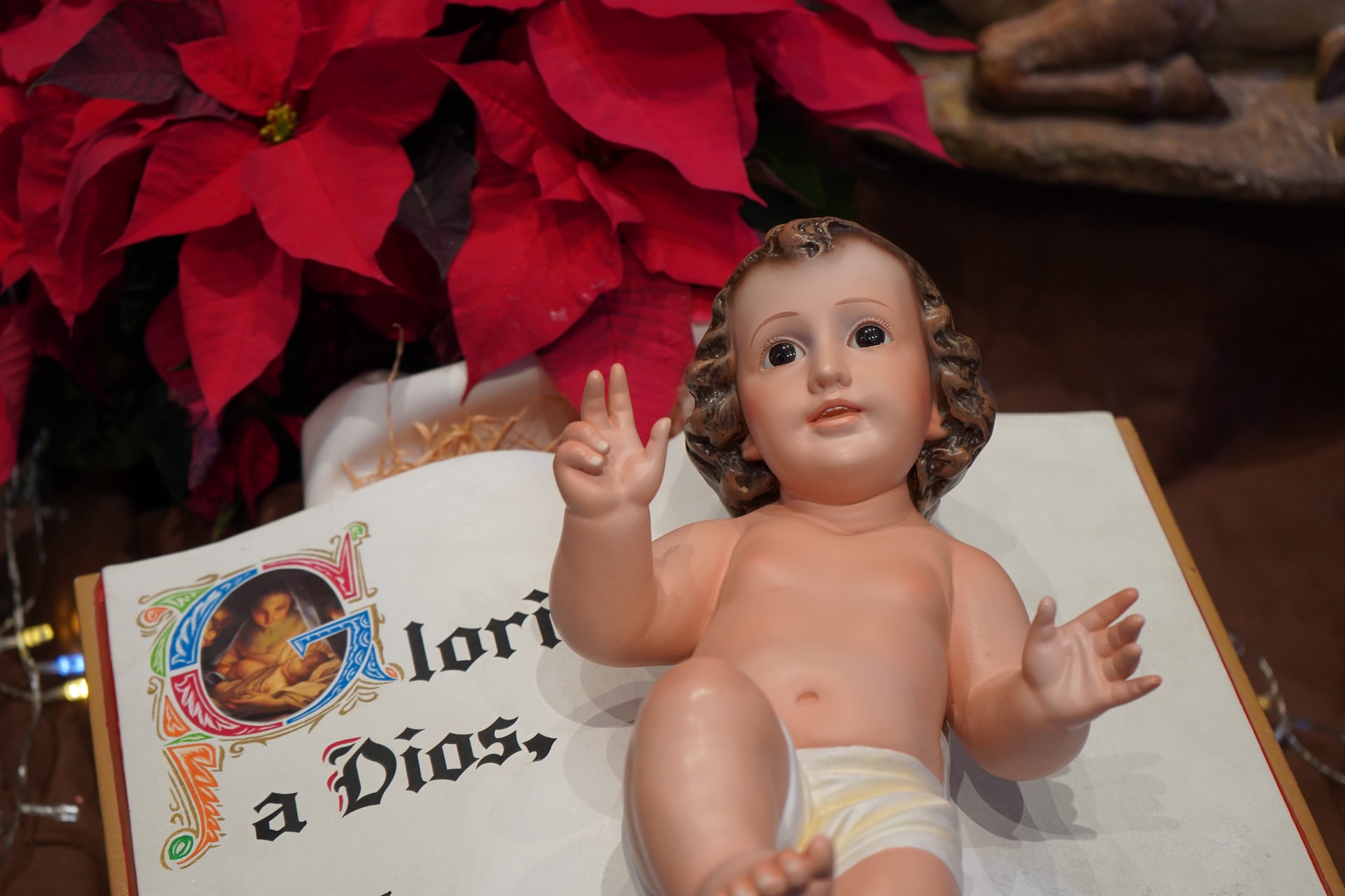 A statue of the Infant Jesus lying on top of a Bible. The Bible is opened to page saying "Glory to God" in Spanish.