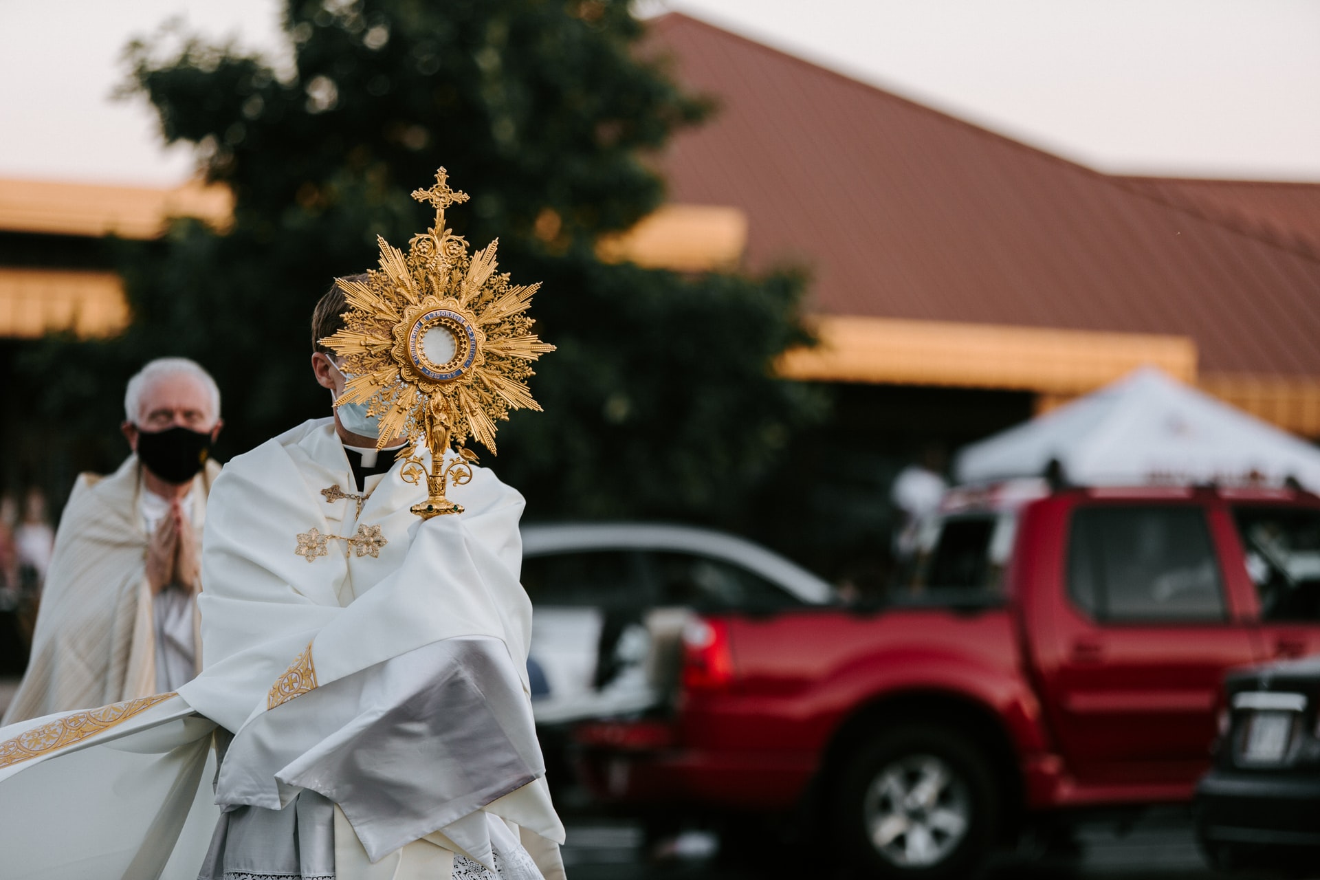 A priest wearing a face mask raises up the Monstrance
